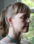 Woman wearing a blue necklace with a blurred outdoor background