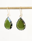 Teardrop-shaped green gemstone drop earrings in gold settings hanging from a gold display rod against a white background.