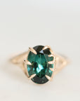 An oval-cut emerald-cut green gemstone ring set in a gold prong setting, shown on a clean white background.