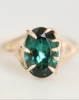 An oval-cut emerald-cut green gemstone ring set in a gold prong setting, shown on a clean white background.