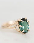 A gold ring with a faceted green gemstone, photographed on a clean, light gray background.