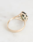 A gold ring with a green gemstone, photographed on a light marble surface.