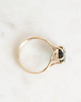 A gold ring with a split shank design and a small dark green rectangular gemstone, photographed on a light marble surface.