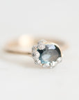 A gold ring featuring a large oval light blue gemstone surrounded by small silver flower-like accents, photographed on a soft white background.