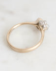 A vintage-style ring with a gold band and a silver-toned floral cluster setting holding small clear stones, photographed on a light marble surface.