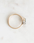 A gold ring with a small clear gemstone in a prong setting, photographed on a light marble surface.