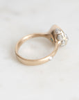 A gold ring with a cluster of small clear gemstones on the setting, photographed on a light marble-like surface.