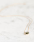 A delicate rose gold necklace with a small oval green gemstone pendant, resting on a white marble surface.