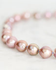 A close-up of a beaded strand bracelet made of iridescent pink baroque pearls strung on a thin blue cord, resting on a light marble surface.