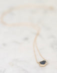 A delicate gold necklace with a raw, irregular dark gray stone pendant, resting on a light marble surface.