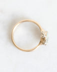 A gold ring with a small cluster of clear gemstones on a light, textured white background.