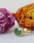 Gold ring with a green gemstone next to dried flowers on a white background