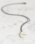 A teardrop-shaped white pendant necklace with hand-painted black symbols, hanging from a dark gray cord on a light marble surface.