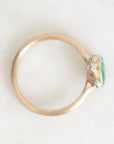 A gold ring with a green oval gemstone and small clear accent stones, photographed from above on a light marble-like surface.