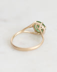 A gold ring with a green gemstone in a prong setting, photographed on a light marble surface.