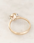 A gold ring with a unique sculptural dome-shaped setting featuring three small clear gemstones, photographed on a light marble surface.