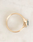 A gold ring with a textured band and a bezel-set oval light blue gemstone accented by small clear stones, photographed on a light marble surface.