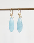 Pair of light blue teardrop earrings on gold hooks against a white background