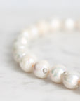 A close-up of a strand of irregular white baroque pearls on a light marble surface, with a small silver spacer bead visible.