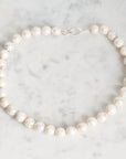 A strand of irregular white freshwater pearls with a silver clasp, arranged in a circle on a light gray and white marble surface.