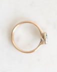 A gold ring with a small cluster of clear gemstones and a tiny light blue accent on the setting, photographed from above on a light off-white surface.