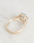 A rose gold ring with a light blue gemstone and small clear accent stones, photographed on a light marble surface.