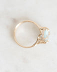 A gold ring with a light blue oval gemstone and small clear accent stones, photographed on a light marble surface.