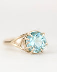 Blue gemstone ring with branchy gold prong setting against a plain background.