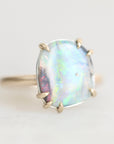 Colorful opal ring with gold prongs against a plain background.