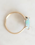 Top down view of opal ring with gold prongs and band against a plain white background.