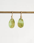 A pair of gold drop earrings with smooth, teardrop-shaped light green stone pendants, hanging from a horizontal gold rod against a plain white background.