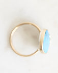 A gold ring with a flat, oval-shaped light blue stone, photographed on a clean white background.
