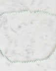 A delicate beaded necklace with alternating light blue and white beads, arranged in a circle on a white marble surface.