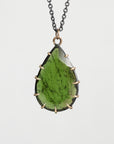 A teardrop-shaped green gemstone pendant necklace with a dark metal chain and a bronze-toned bezel setting, shown against a light gray background.