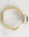 A gold ring with a dark blue oval center stone and three small clear accent stones, photographed from above on a light marble-like surface.