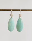 Teardrop-shaped green earrings with silver hooks on a light gray background