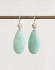 Pair of light green teardrop earrings with silver hooks on a white background