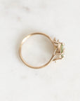 A gold ring with a small green gemstone, photographed on a light marble surface.