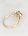 A gold ring with a bezel-set rectangular blue gemstone, photographed on a light marble surface.