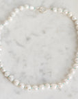 A strand of irregular white freshwater pearls with small turquoise blue spacer beads, arranged in a circle on a light gray marble surface.