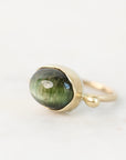 A gold ring featuring a large oval green cat's eye stone, photographed on a clean white background.