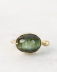 A gold ring featuring an oval green labradorite stone with natural iridescent shimmer, set against a clean white background.