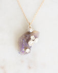Bright purple fossilized opal with silver rose details suspended from a gold chain against a marble background.