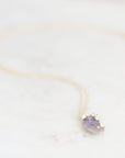 Bright purple fossilized opal with silver rose details suspended from a gold chain against a marble background.