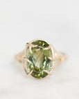 An oval-cut green gemstone ring set in a gold-toned band with a claw-style prong setting, photographed on a clean white background.