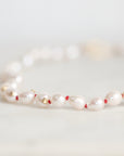A close-up of a beaded necklace featuring irregular white pearls separated by tiny red beads and accented with small gold spacers, resting on a light marble surface.