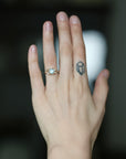 A close-up of a person's hand wearing a delicate gold ring with a round light blue gemstone, set against a dark, blurred background.