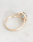 A gold ring with a small light blue gemstone, photographed on a light marble surface.