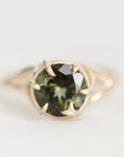 A gold ring featuring a round faceted dark green gemstone held in a prong setting, photographed on a clean white background.