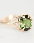 A gold ring featuring a round green gemstone in a prong setting, photographed on a clean white background.